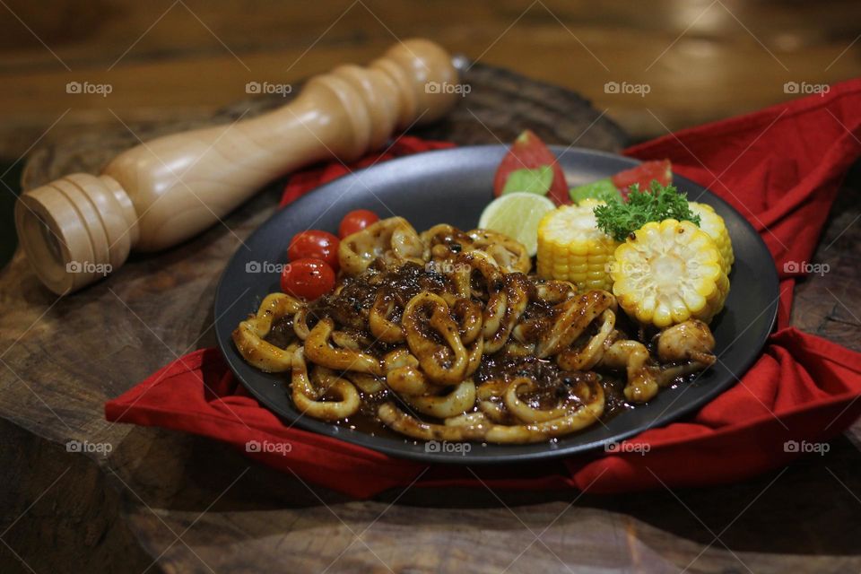 Close-up portrait of squid rings seasoned with barbecue sauce served on a black plate on a wooden table, wooden barbecue spice shaker background — Stock Photo