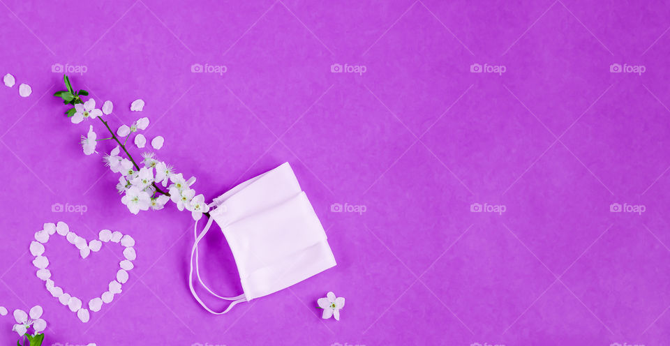 White protective mask and cherry flowers on purple background with copy space. Concept of fight against coronavirus covid-19. Concept of hope.