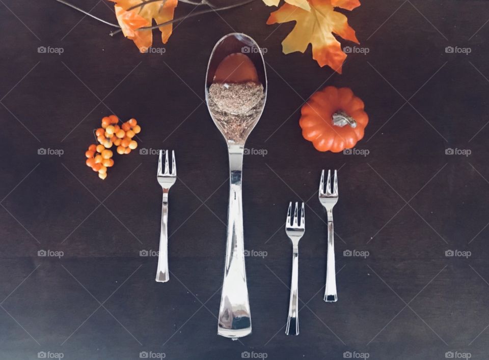 Beautiful table top display for the fall season large silver spoon with an acorn inside , surrounded by mini silver forks and holiday berries, mini orange pumpkin and autumn leaves- orange, red, brown, green and yellow, and gold 
