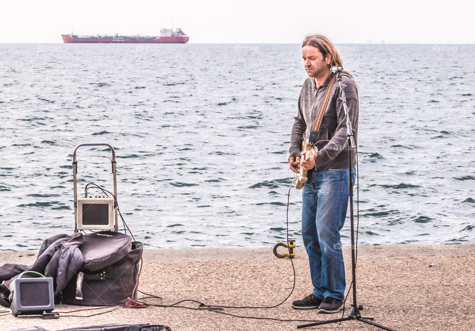 Young Man Electric Guitar Music Guitarist Player With His Audio Equipment Performing In The Street In The Front Of The Sea
