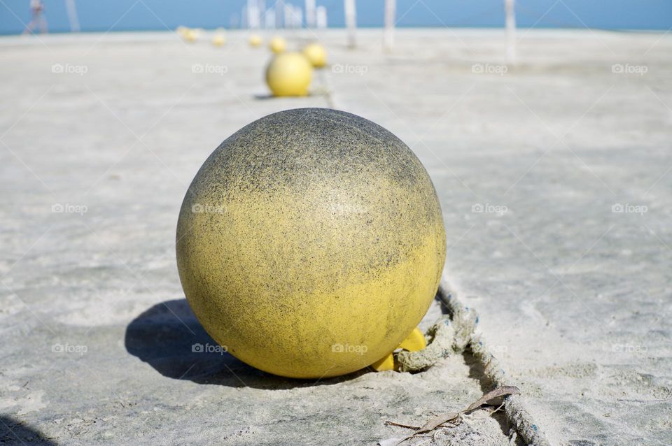 A line of weathered yellow buoys on the beach.