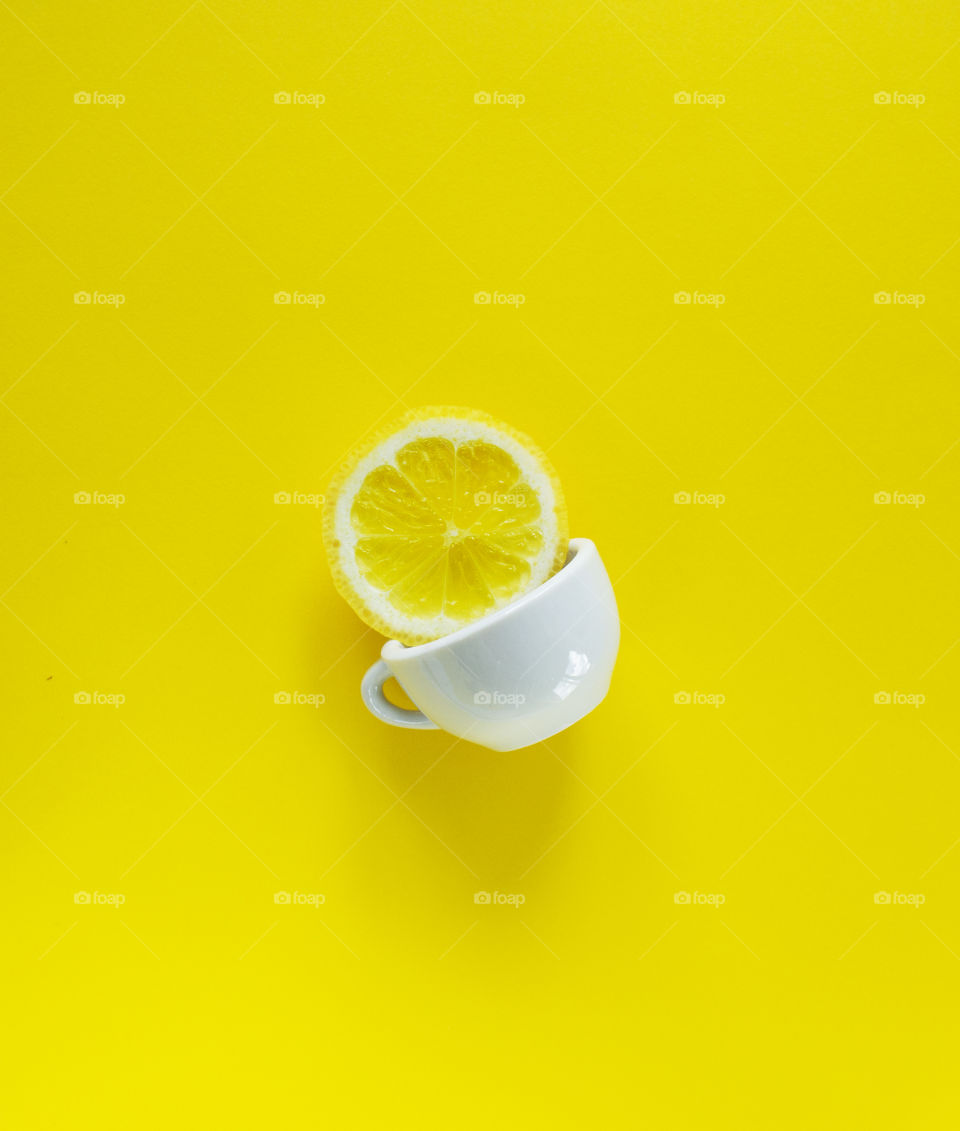 Yellow splash. A slice of lemon and white cup on a yellow background 