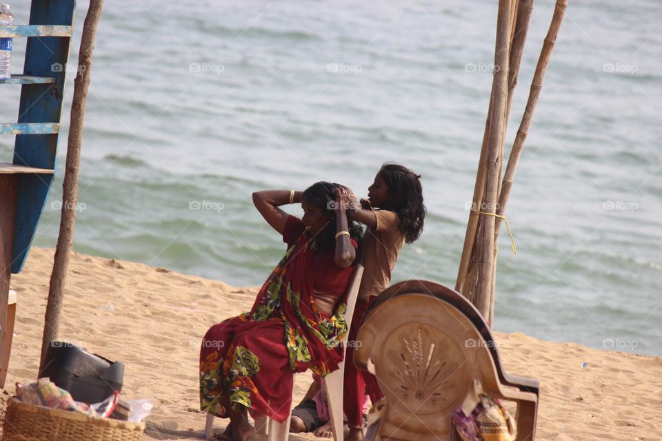 This picture was described about a mother and daughter,
the daughter is dressing and making hair of her mother over the beach
