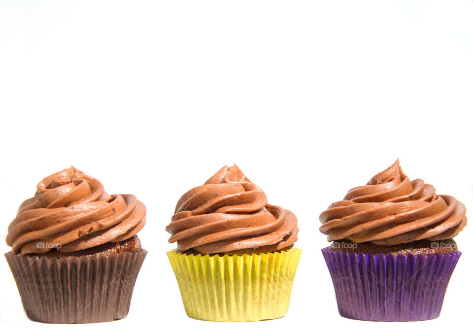 Three Chocolate Cupcakes. A row of three cupcakes with colourful cases which are isolated on a white background.