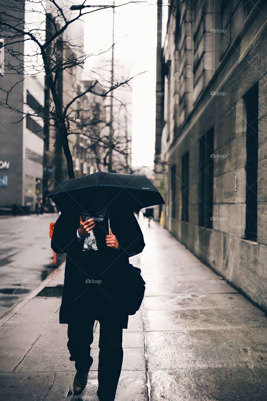 Inopportune phone call while walking down the street covering myself from the rain with a black umbrella.