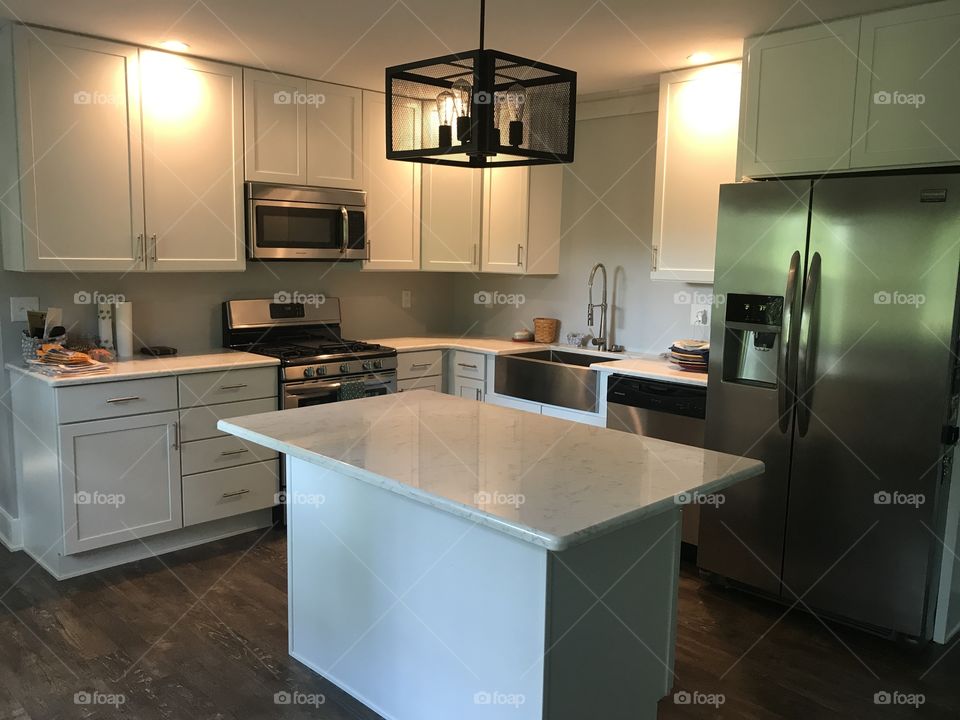 Clean, crisp farmhouse kitchen with stainless steel appliances and quartz countertop with grey veining. 