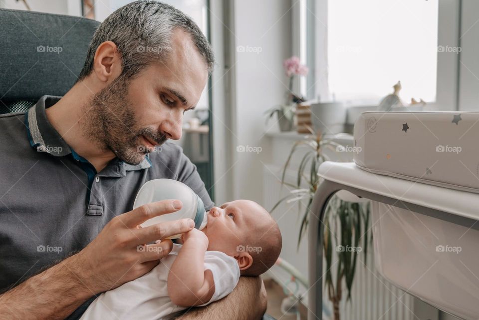 Father feeding his baby son with bottle of baby formula