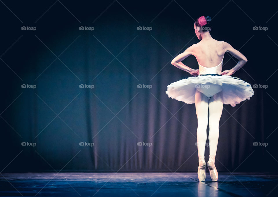 Young Woman Ballerina Dancer On Stage In Dark Background
