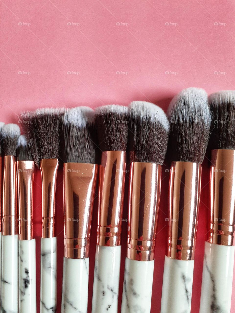 Makeup brushes in varying sizes, some shorter some taller. Some thinner and some thicker in a line on a pink background.