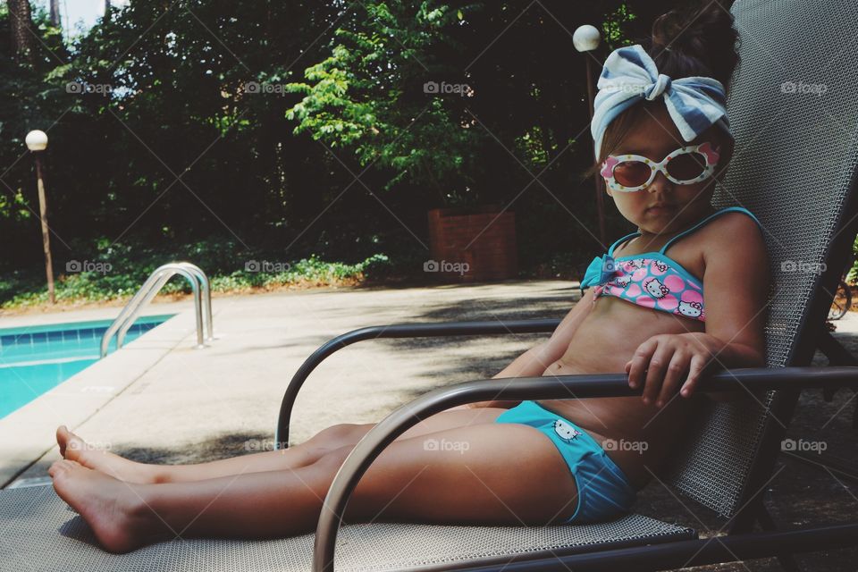 Little girl sitting on lounge near swimming pool