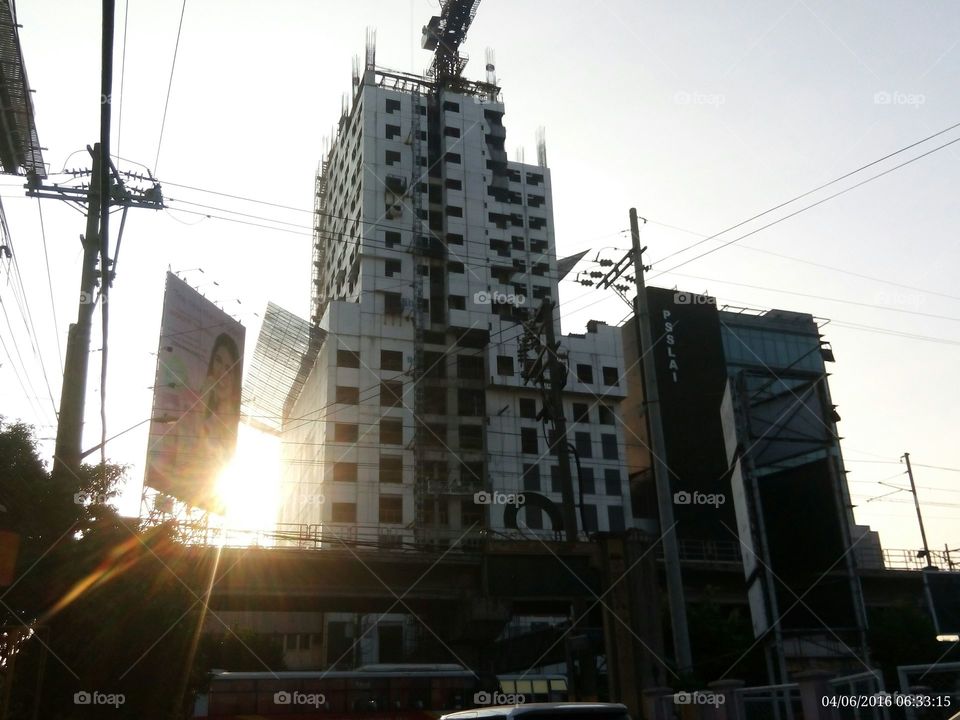 The early morning sunlight passes through a billboard and a building in construction. It symbolizes the hope that every endeavor will ultimately end.