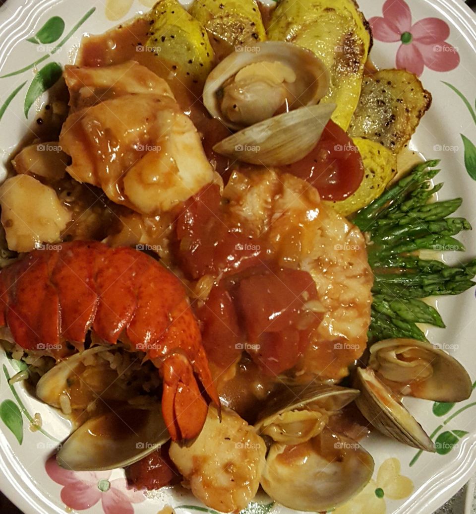 Seafood medley of Lobster, scallops, littleneck clams,  and haddock simmered in a tomato, white wine, saffron infused broth reduction, served over oven roasted asparagus spears and pan fried (in butter,) planks of summer squash.