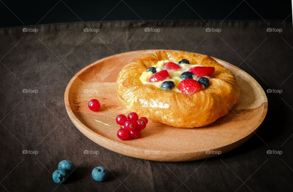Homemade cakes with berries on a dark background. Appetizing fresh denish with cream, strawberries, blueberries and currants on a wooden tray. Autumn mood