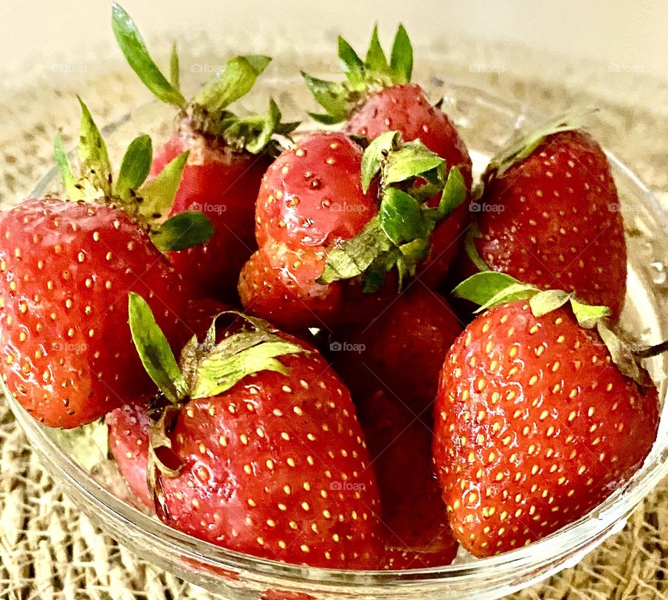 The photo shows a vase filled with fresh strawberries. The strawberries look ripe and delicious, some with green leaves on the tops.