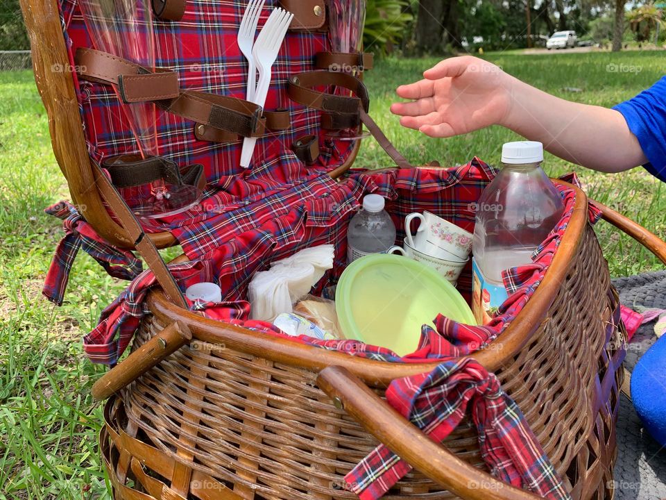 Picnic Basket Opened Up With Food And Items Needed For The Picnic Meal As A Family With A Hand About To Grab Something Or Showing The Basket.