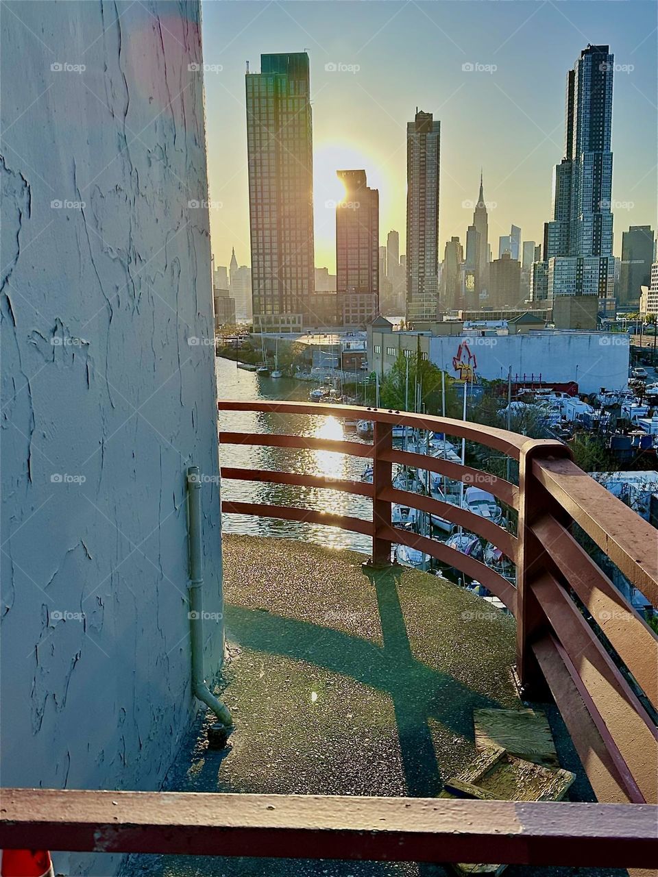 This is the central outpost of the „Pulaski Bridge“ at „Newtown Creek“ that connects LIC to „Greenpoint“, Bklyn in the setting evening sun. Straight ahead in the distance we see „Manhattan“ incl. the „Empire State Bldg“. 2024. Hypnotic Productions