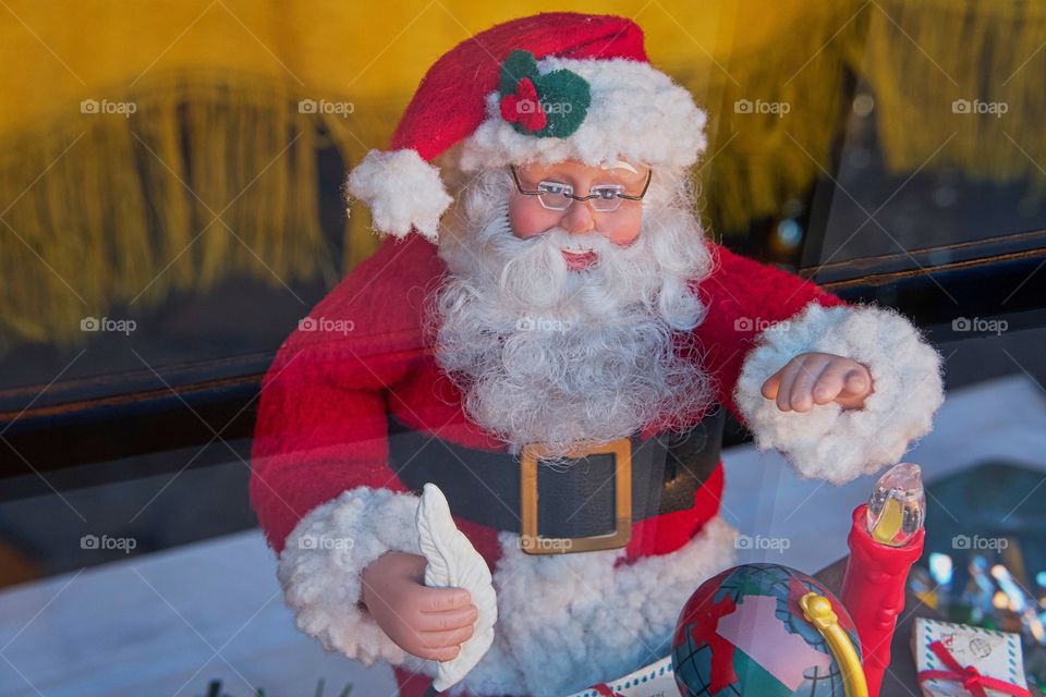 An image of a Santa Claus doll at his desk captured through a storefront window display.
