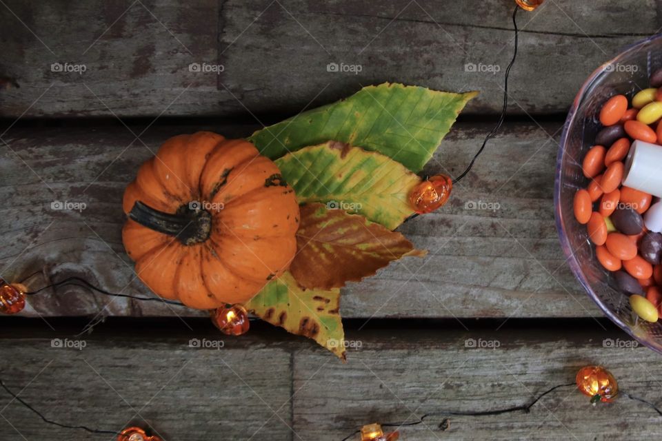 Pumpkin with fall leaves and orange candy in dish on wooden background 