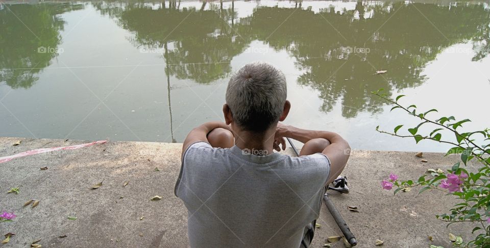 A back view of a man seated along the canal relaxed and fishing in Bangkok, Thailand.