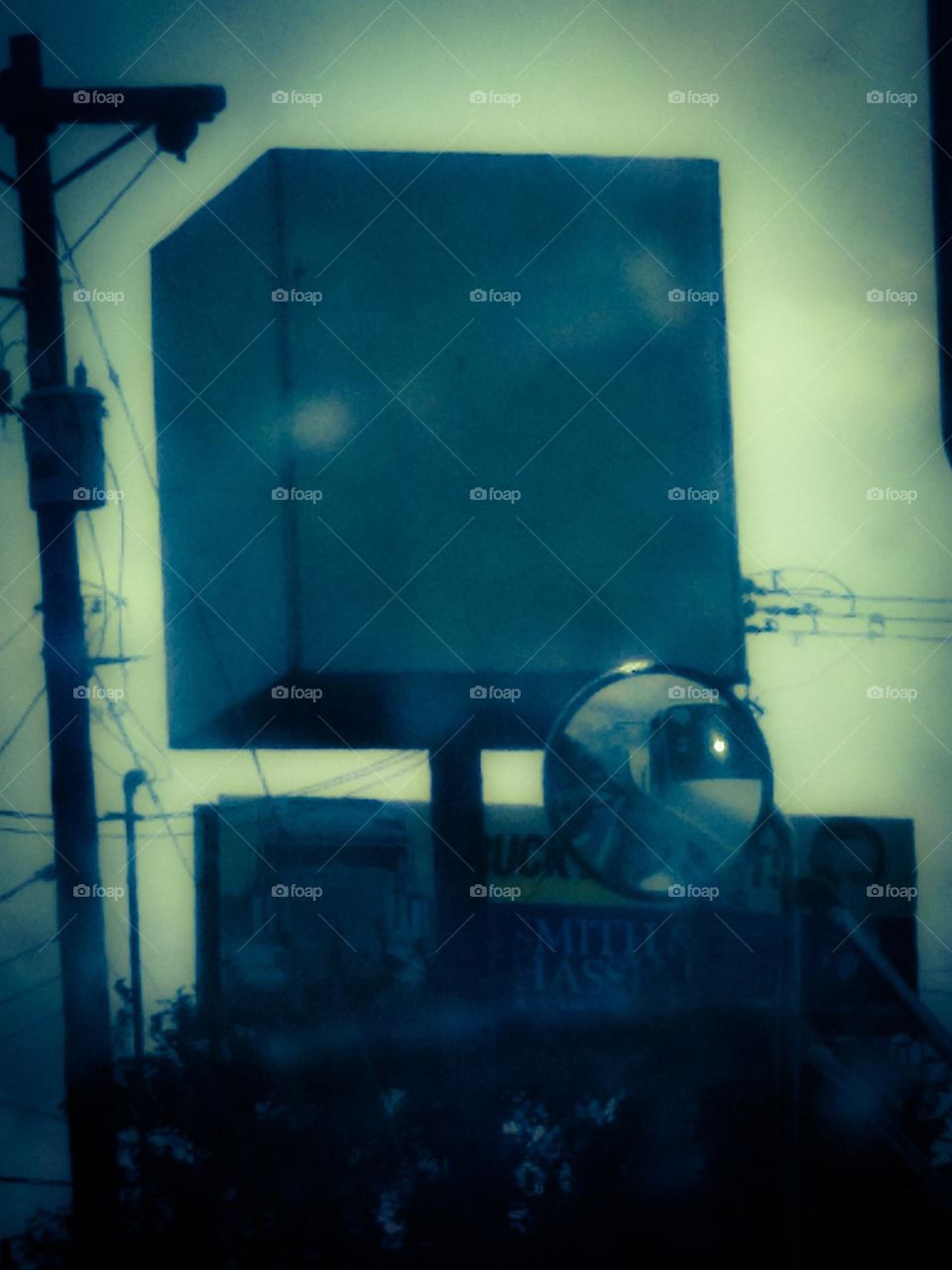 A picture of a large cube in front of a billboard and next to an electrical pole. It was cloudy that day.