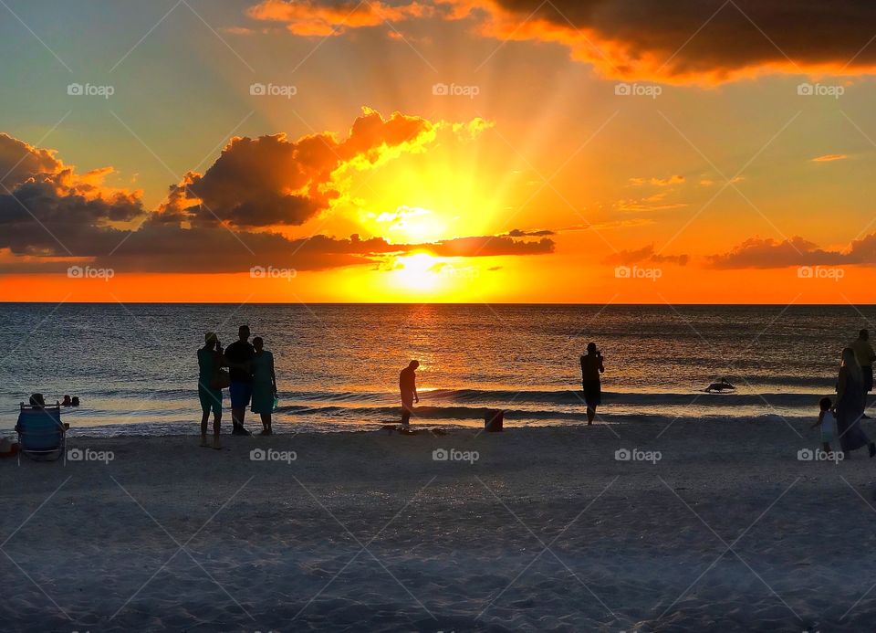 Beachcombers gather to watch a dazzling red and yellow sunset.