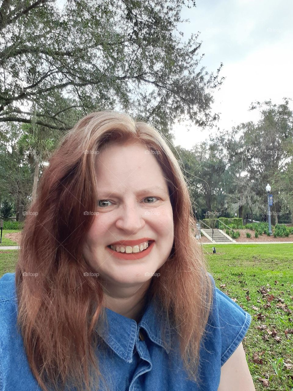 A middle aged caucasian woman with long brown hair takes a selfie while at Lake Lily Park in Maitland, Florida.