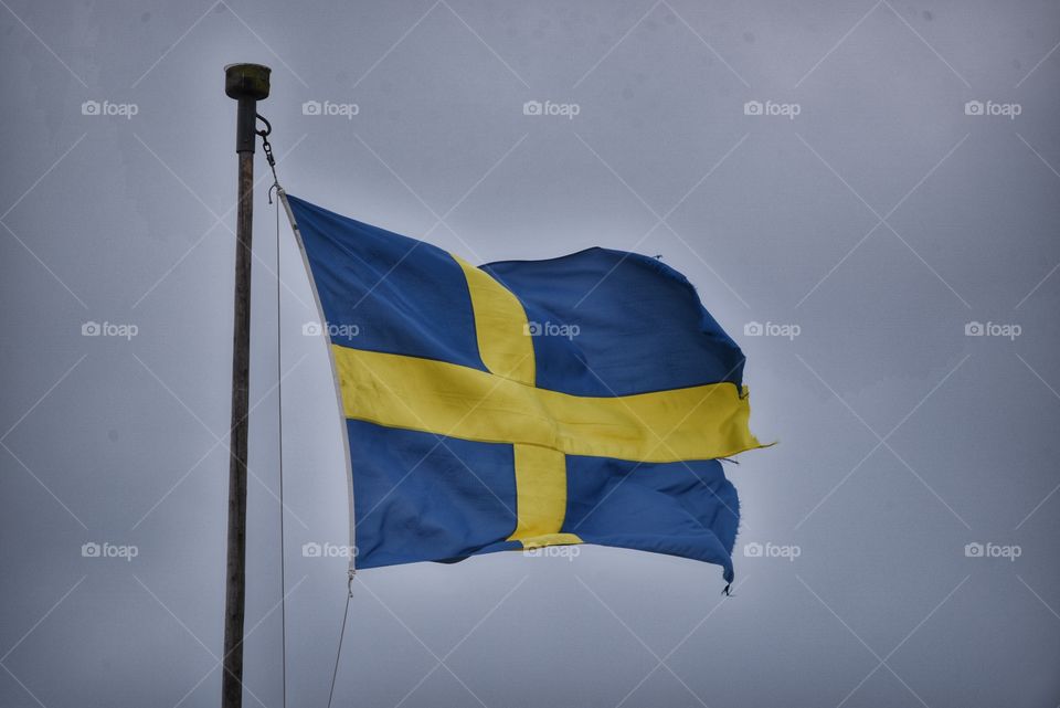 Torned swedish flag waving in the grey sky during an autumn day