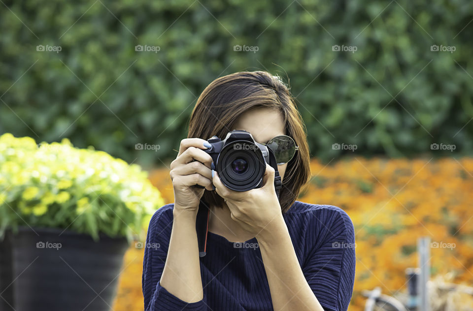 Hand woman holding the camera Taking pictures Background of trees and flowers