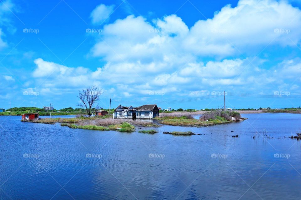 The blue water and sky are the same color, and the house and tree in the lake are beautiful and very artistic