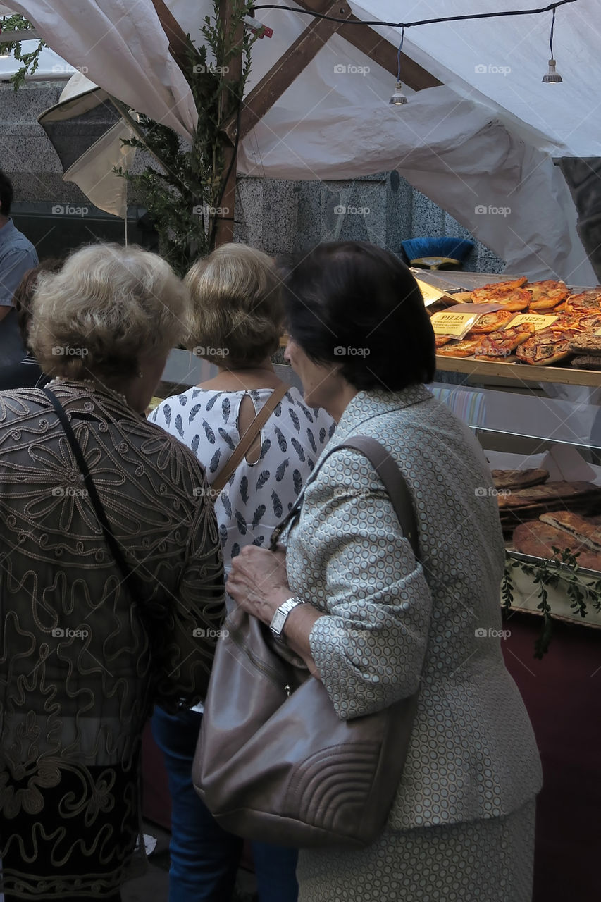 Older women looking at comfort food that street vendors sell at an open air  market in the center of Barcelona, Spain.
