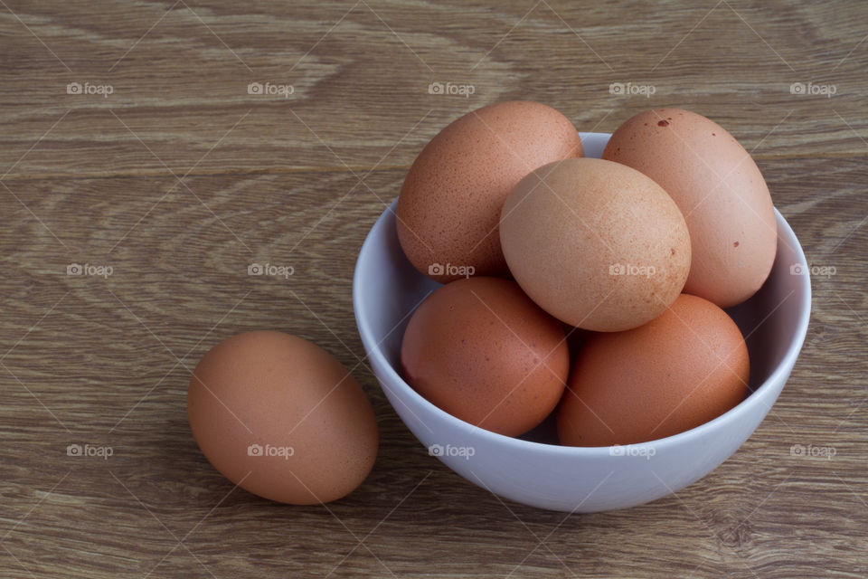 A bowlful of fresh, brown speckled hen eggs on a wooden table. Simple food shot of eggs.