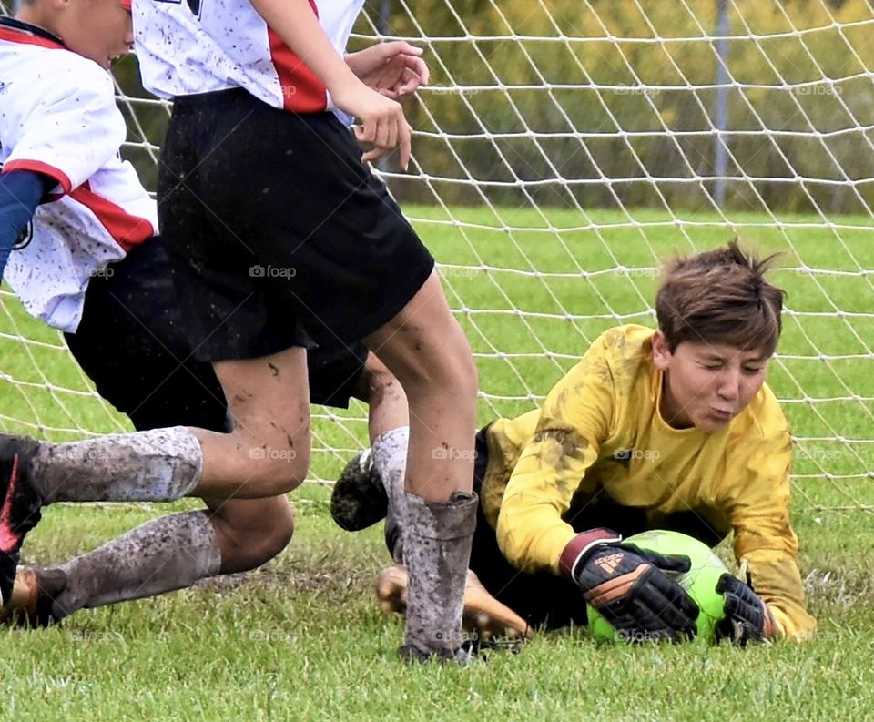 Soccer goalie grabbing the ball in a muddy game