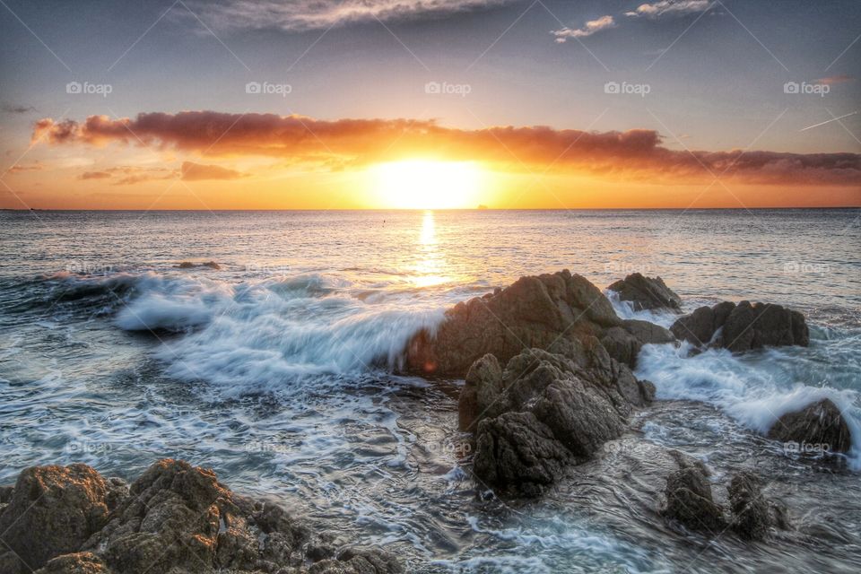 Early morning sunrise at the coast. A view of the ocean with the sun rising over rocks at the coast.