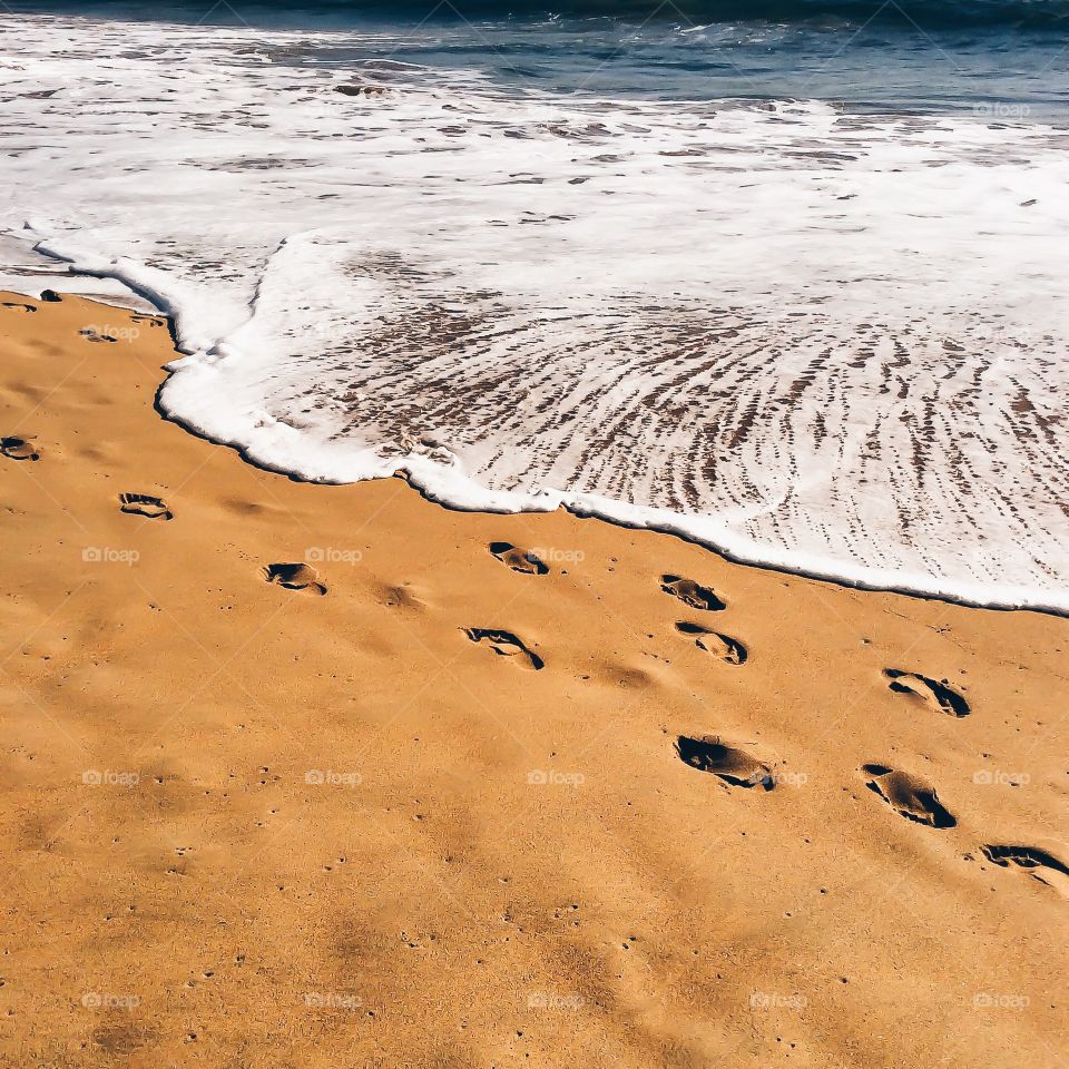 Footprints in the sand, and the oncoming ocean wave