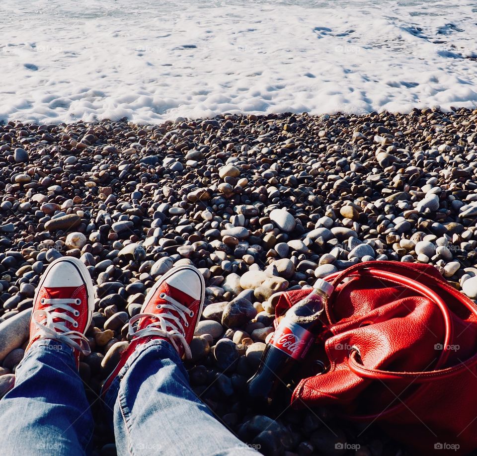 A bottle of Diet Coke on the beach with a red leather bag and red sneakers.