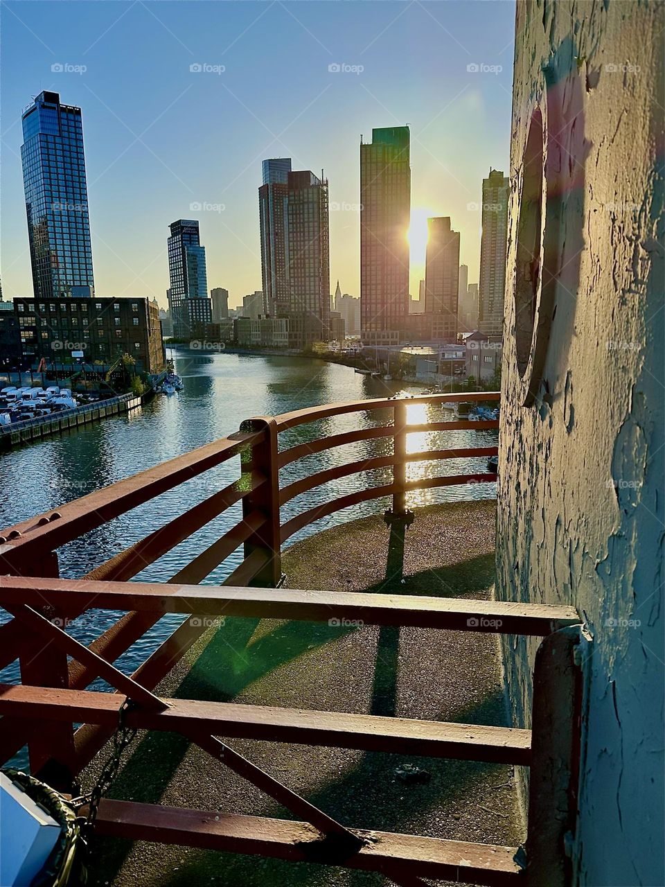 This is the center outpost of the “Pulaski Bridge” at “Newtown Creek” that connects “Greenpoint”, Bklyn to LIC, Queens in the warm light of the setting sun. Across the shimmering “East River” we see LIC and “Manhattan”. 2024. Hypnotic Productions