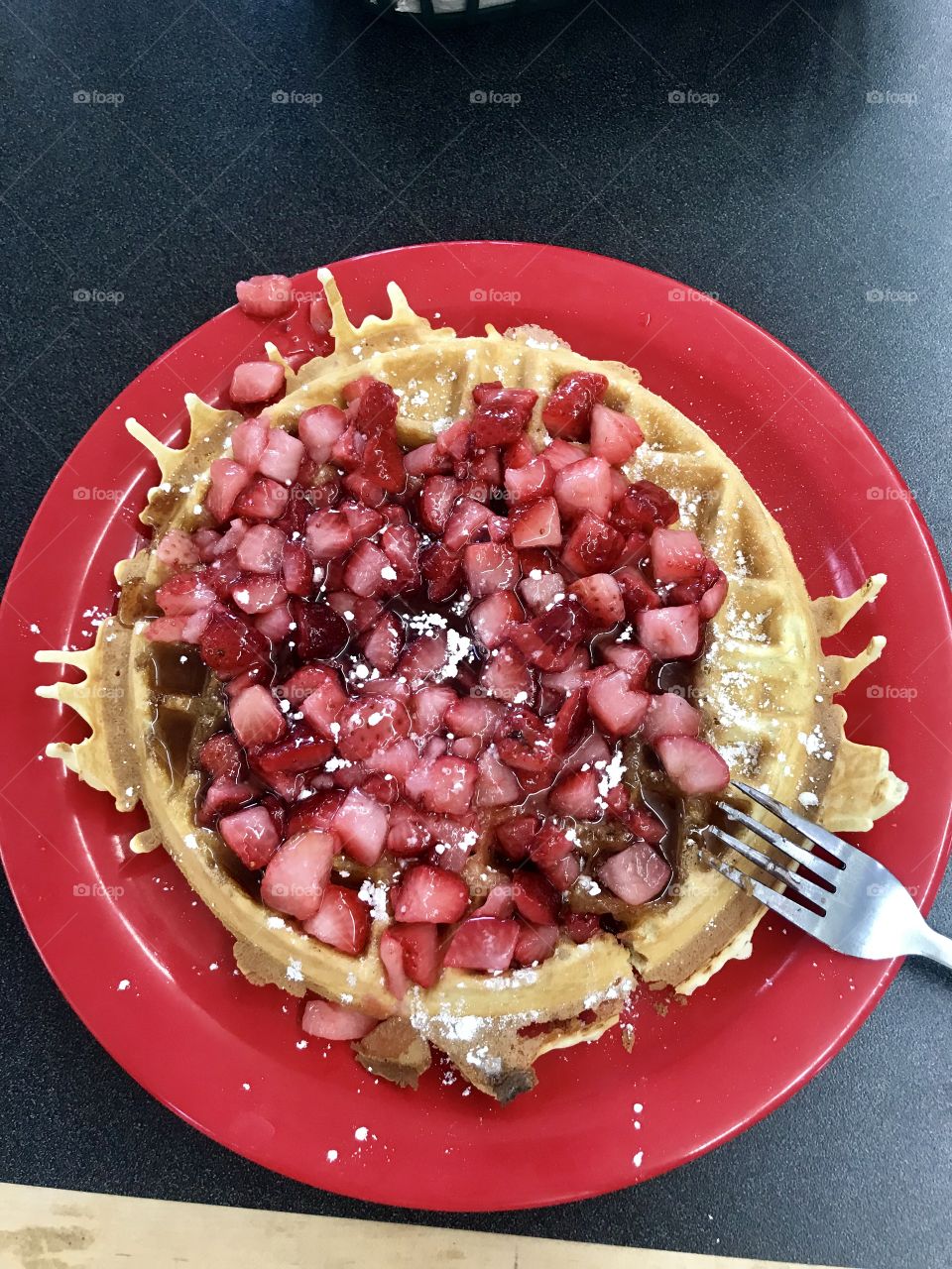 Colorful image of a large golden brown waffle covered in powdered sugar and strawberry toppings