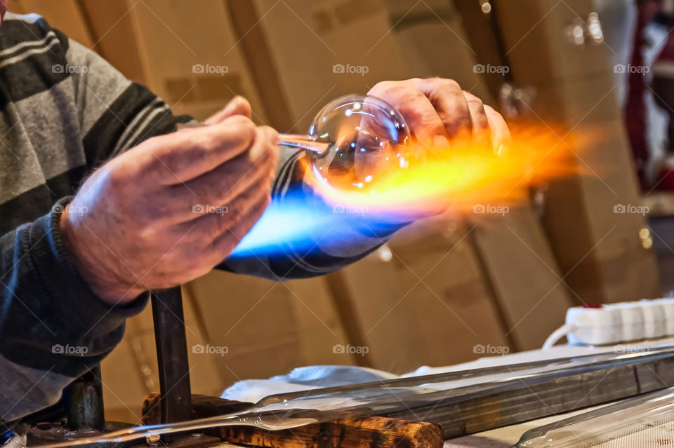 Glassblower forming round shaped Christmas bauble using gas jet flame.