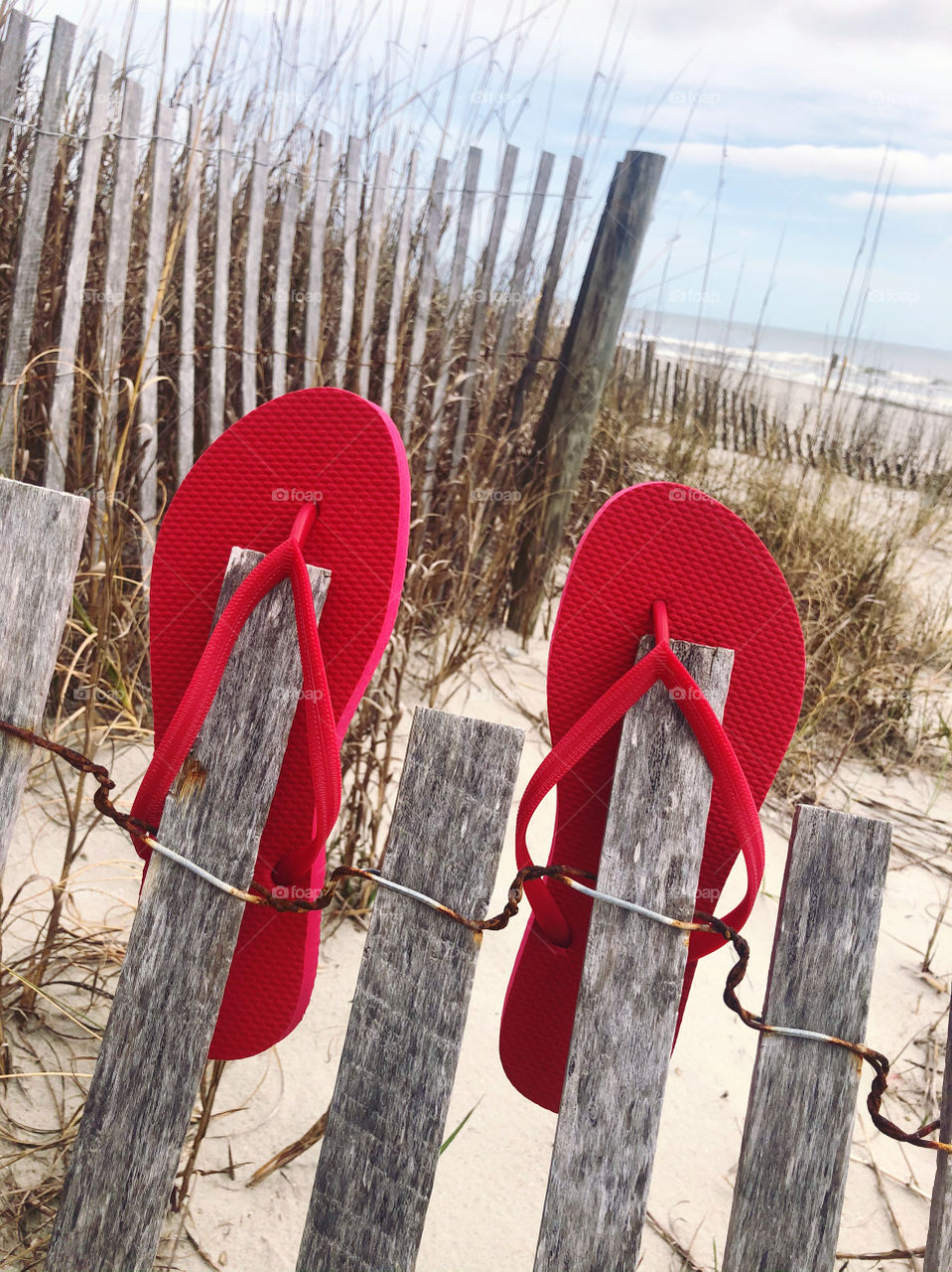 Red flip flops on a beach fence. 