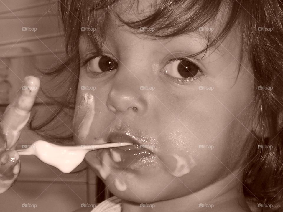 Brown, big eyed girl. Little girl is smudging her icecream al over her face and looks with her big Brown eyed