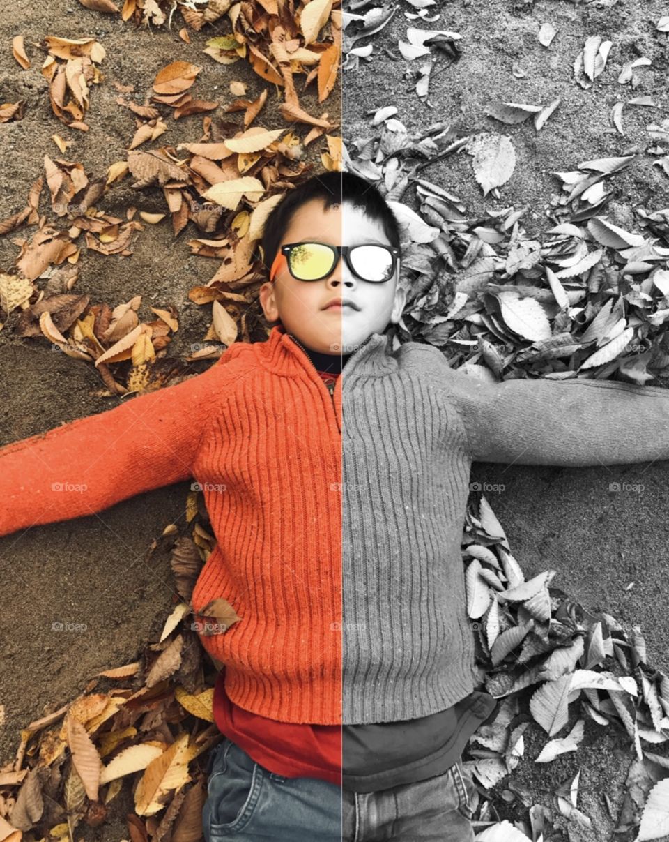 A young boy lying in autumn leaves in colour and b&w