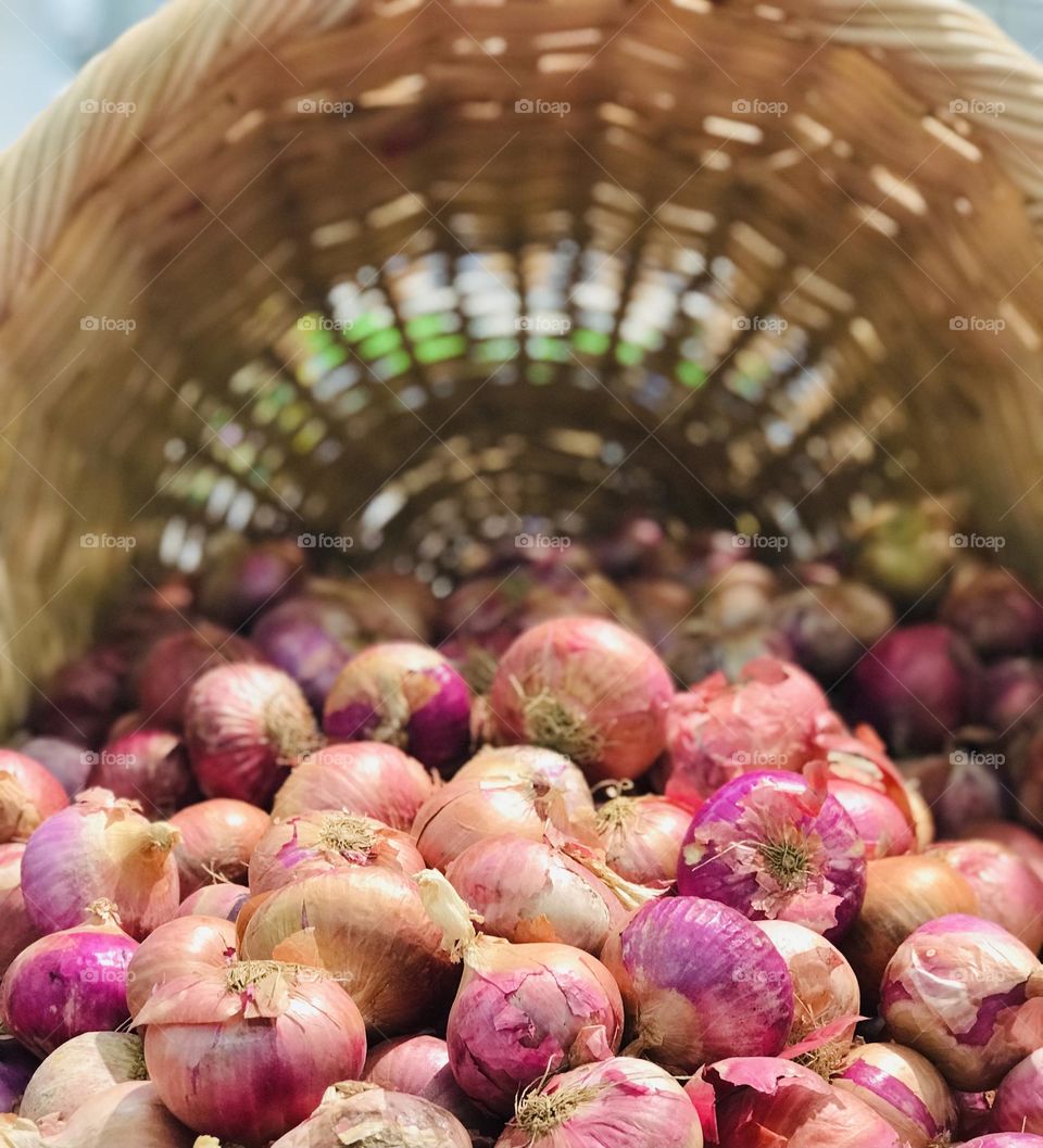 A flatten bamboo basket full of onions.