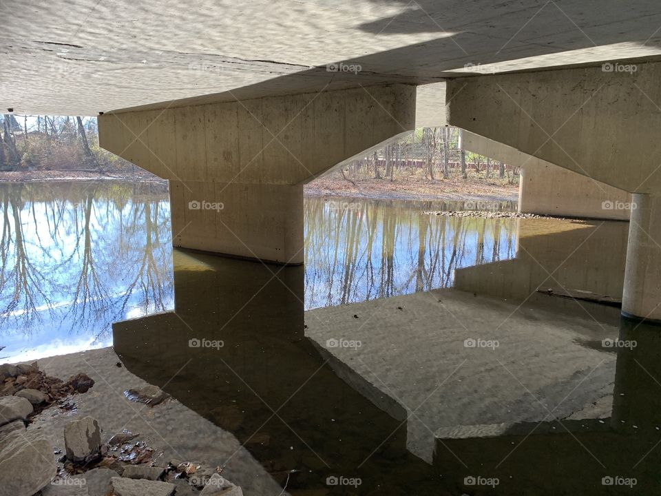 A bridge over tame waters. These waters are just about clear enough to see to the bottom. I can see my reflection clearly, as well as the rocks beneath.