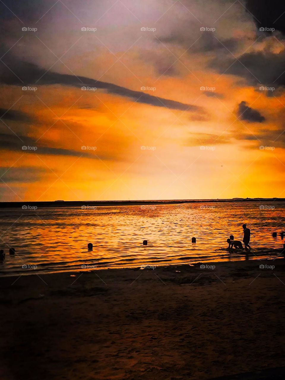 Portrait of a beautiful sunset view on the beach. The orange and yellow sky reflects its light onto the surface of the water