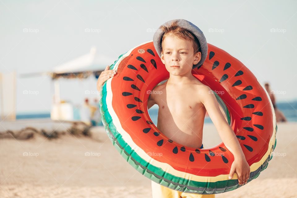 A little boy with watermelon swimming circle at the beach