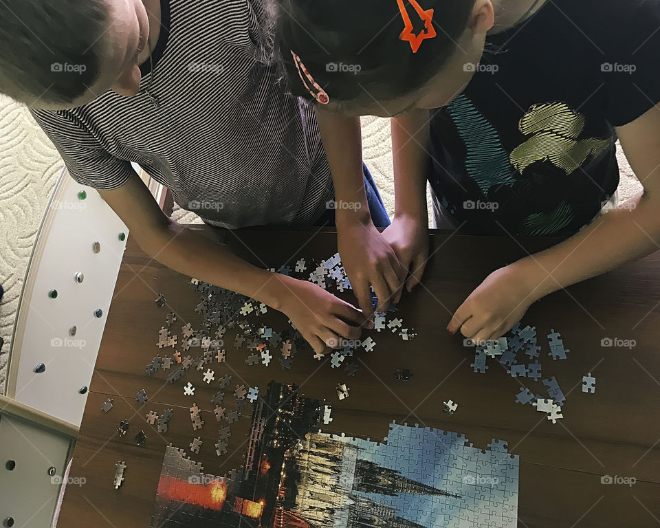 Children gathering puzzles together at home on wooden table 