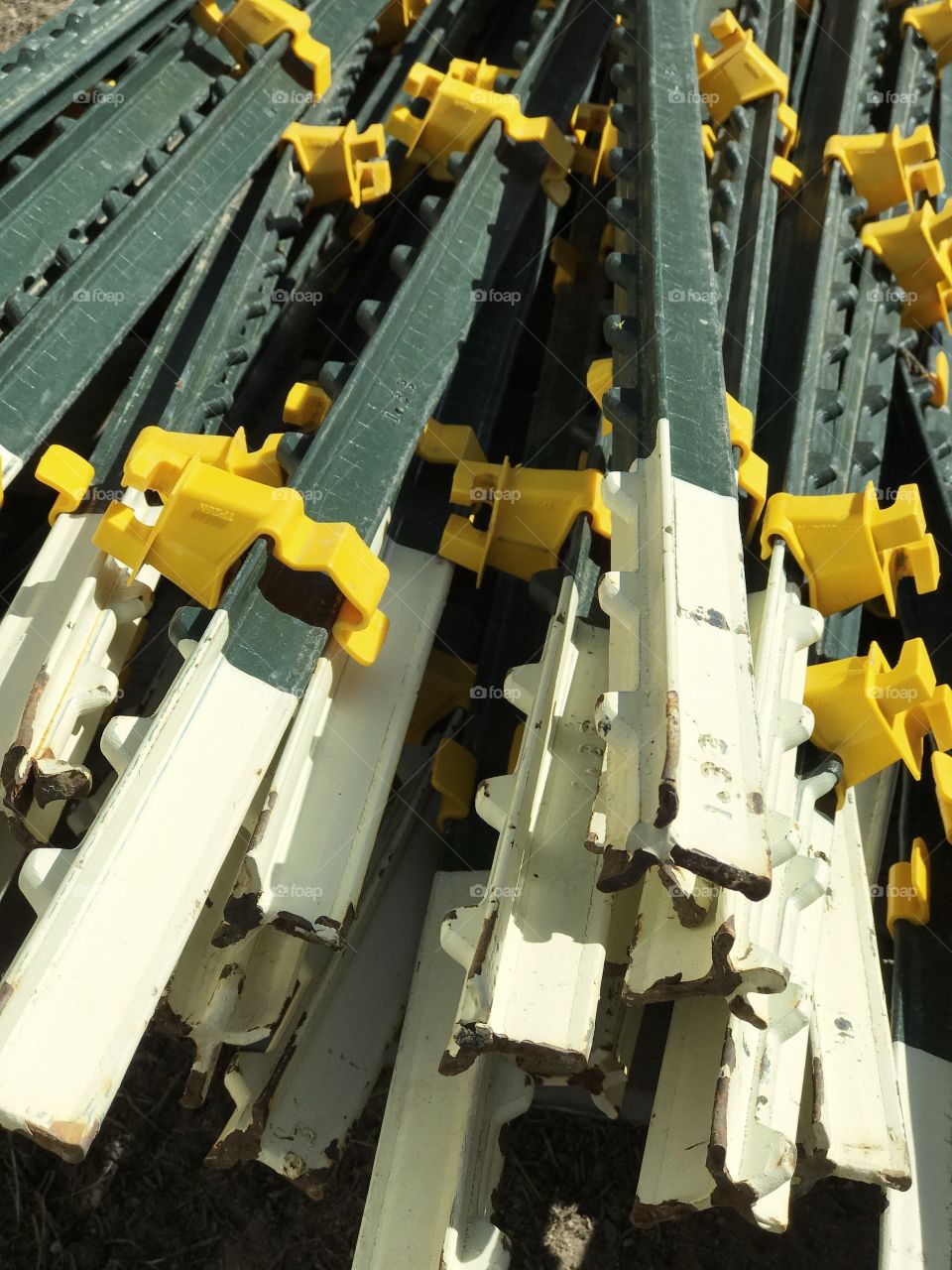 A pile of green and white fence posts with yellow wire clips attached out on a ranch n a sunny day. 
