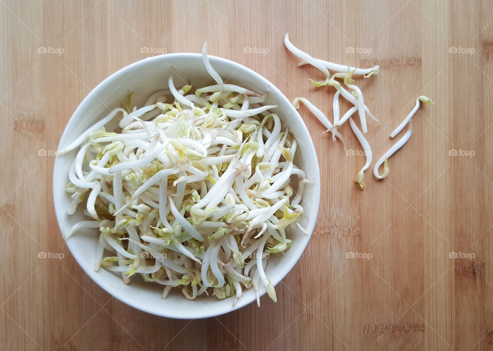 Fresh and clean mung bean sprouts in the white bowl with some outside - Top view from wooden kitchen counter top