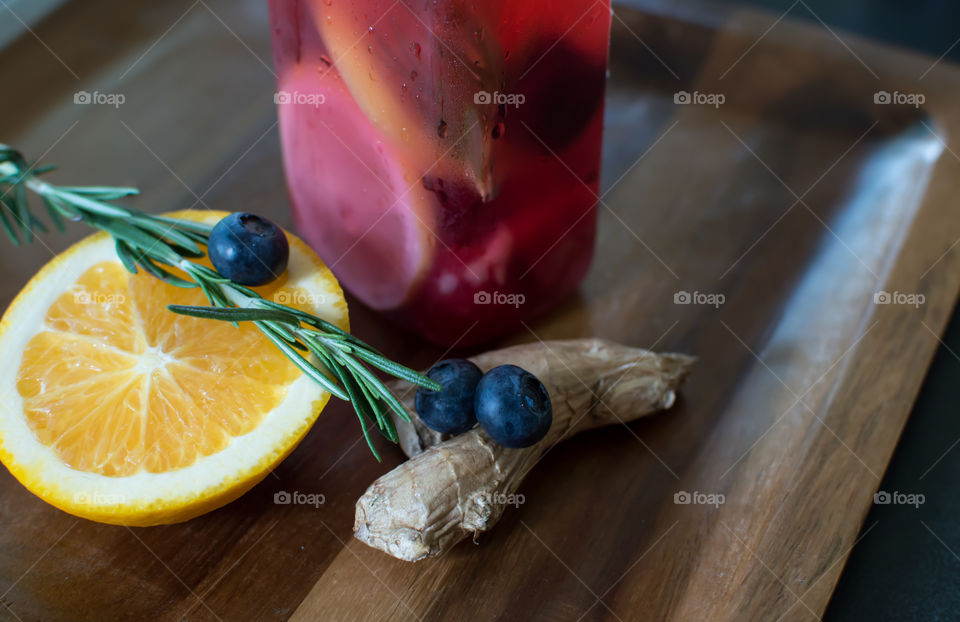 Aromatic and healthy summer drink on dark wood tray with ingredients for wellbeing and healing are ginger root, antioxidant blueberry, aromatic rosemary herb and vitamin rich sliced orange 