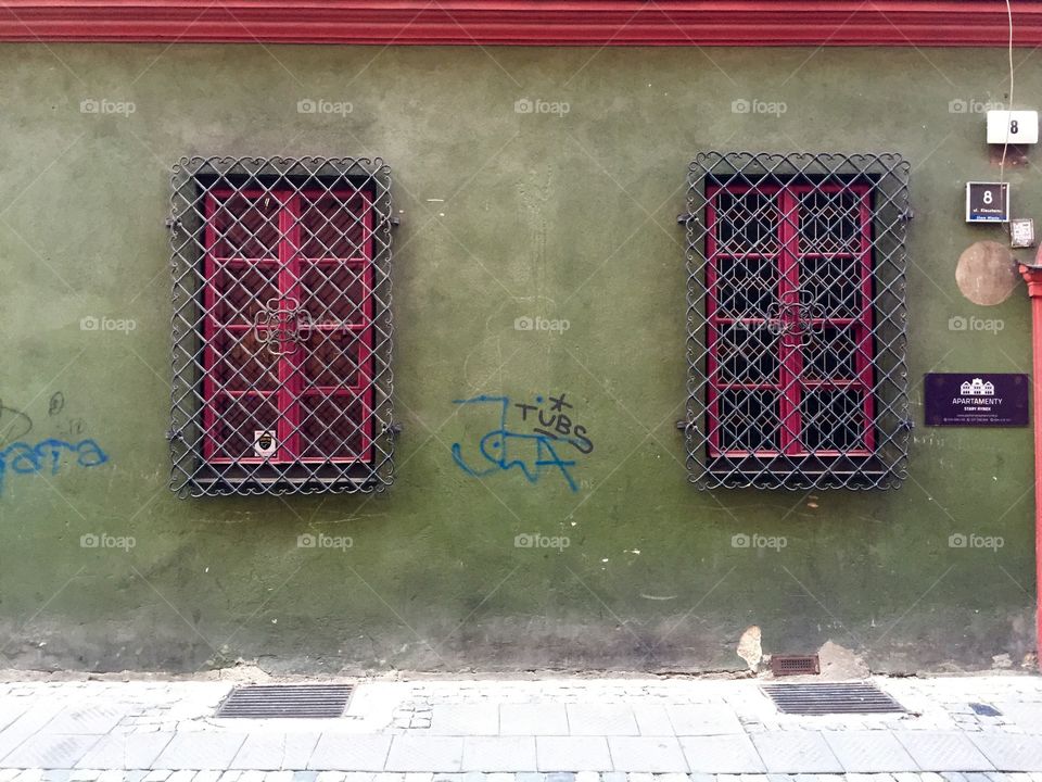 Green wall with fuchsia colored windows with grating